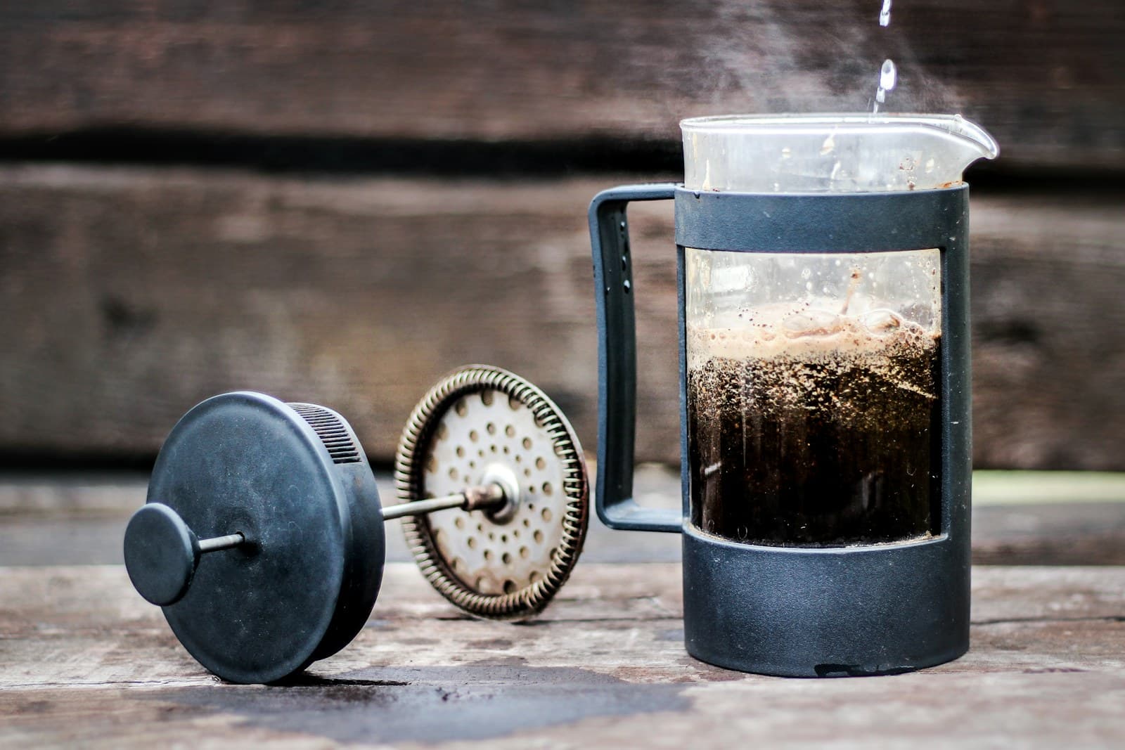 A well-used French press steaming on a rustic wooden table
